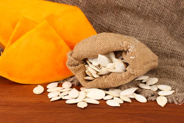 Pumpkin seeds in sack, on wooden background — Stock Photo, Image