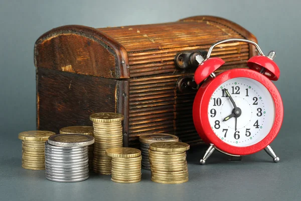 Reloj despertador con monedas en el pecho sobre fondo gris — Foto de Stock