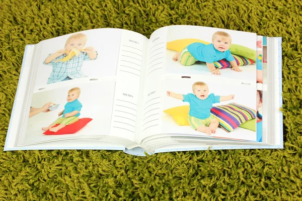 Open photo album with pictures on green carpet — Stock Photo, Image