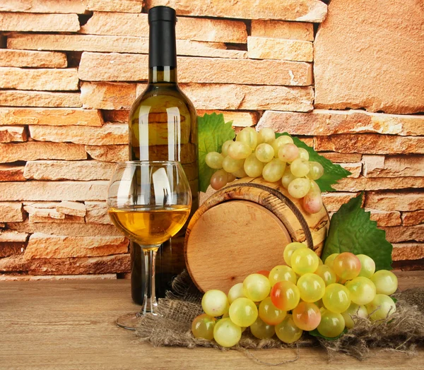 Composition of wine and grapes on wooden barrel on table on brick wall background — Stock Photo, Image