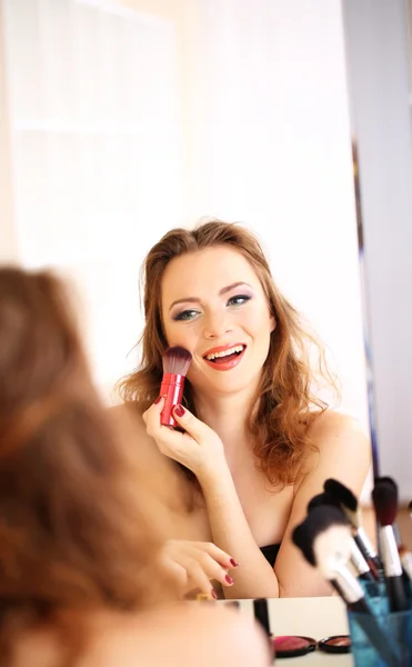 Joven hermosa mujer haciendo maquillaje cerca del espejo —  Fotos de Stock