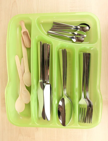Green plastic cutlery tray with checked cutlery and wooden spoons on wooden table — Stock Photo, Image