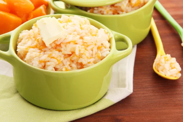 Taste rice porridge with pumpkin in saucepans on wooden background — Stock Photo, Image