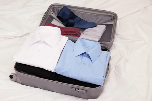 ベッドの上の服と灰色のスーツケースを開く — ストック写真