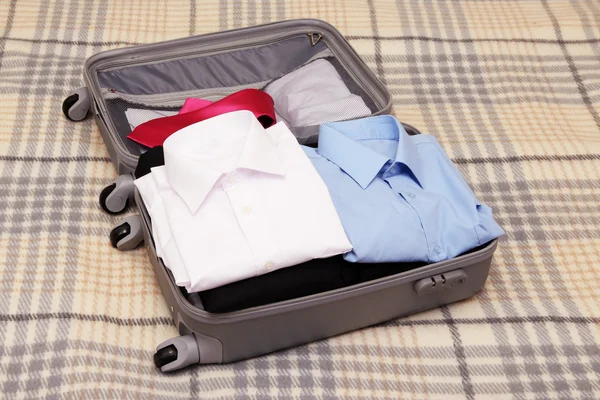 Open grey suitcase with clothing on plaid — Stock Photo, Image