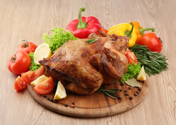 Whole roasted chicken with vegetables on plate, on wooden table — Stock Photo, Image