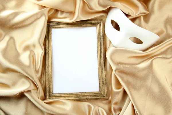 White mask and empty frame on golden silk fabric — Stock Photo, Image