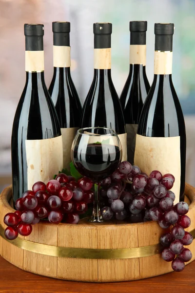 Composition of wine bottles, glass and grape,on wooden barrel, on bright background — Stock Photo, Image