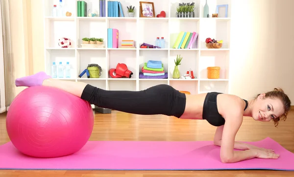 Jonge vrouw doen fitness oefeningen met gymnastiek bal thuis — Stockfoto