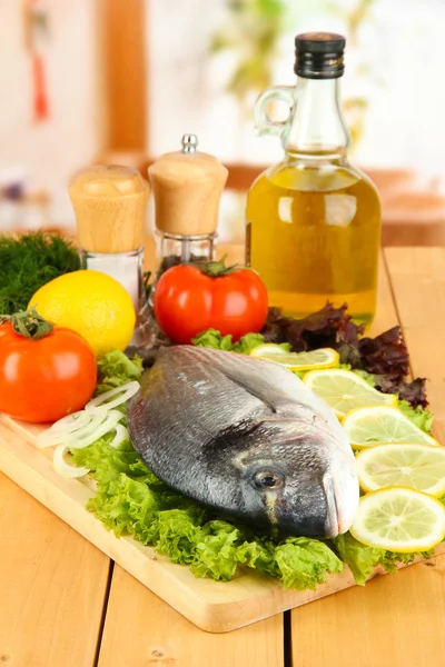 Fresh dorado on chopping board with lemon and vegetables on wooden table — Stock Photo, Image