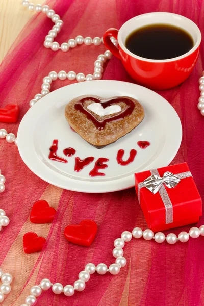 Kue coklat dalam bentuk hati dengan secangkir kopi di atas taplak meja merah muda close-up — Stok Foto