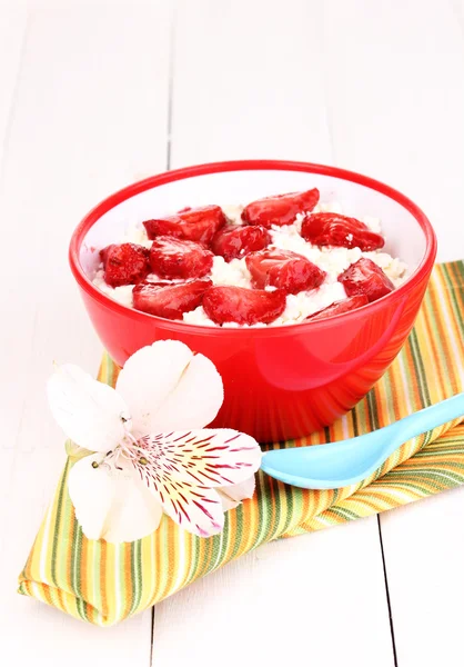 Cottage fromage dans un bol rouge avec des fraises tranchées sur table en bois blanc — Photo