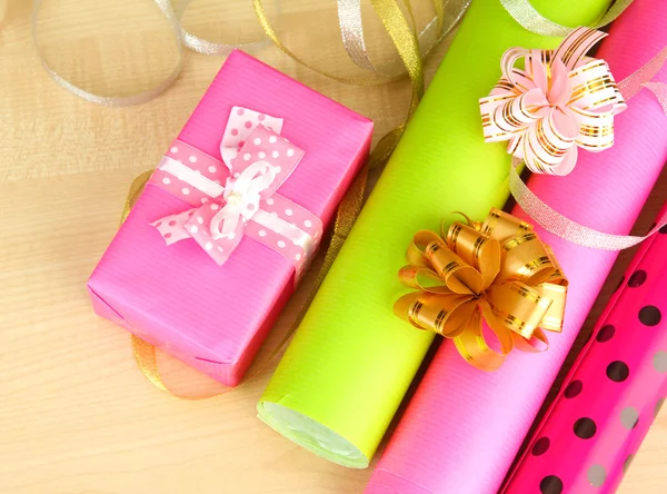 Rolls of Christmas wrapping paper with ribbons, bows on wooden background — Stock Photo, Image