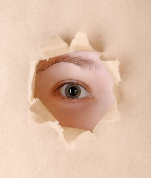 Vrouwelijke oog op zoek door gat in vel papier — Stockfoto