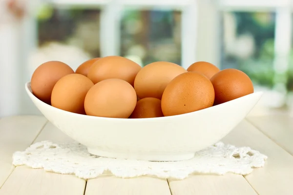 Eggs in white bowl on wooden table on window background — Stock Photo, Image