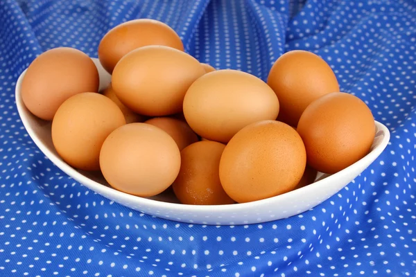 Huevos en tazón blanco sobre mantel azul de cerca — Foto de Stock