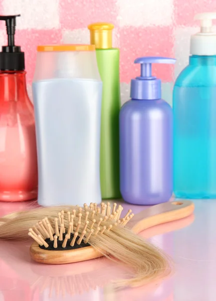 Brosse peigne avec cheveux et bouteilles cosmétiques dans la salle de bain — Photo