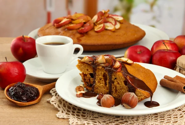 Fatia de torta caseira saborosa com chocolate e maçãs e xícara de café, na mesa de madeira — Fotografia de Stock