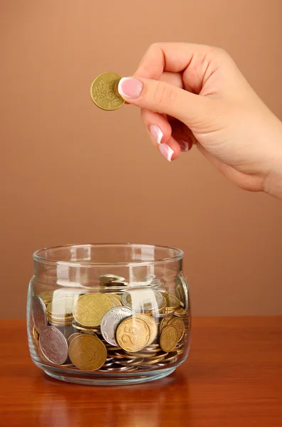 Poupança, mão feminina colocando uma moeda em garrafa de vidro, em fundo de cor — Fotografia de Stock