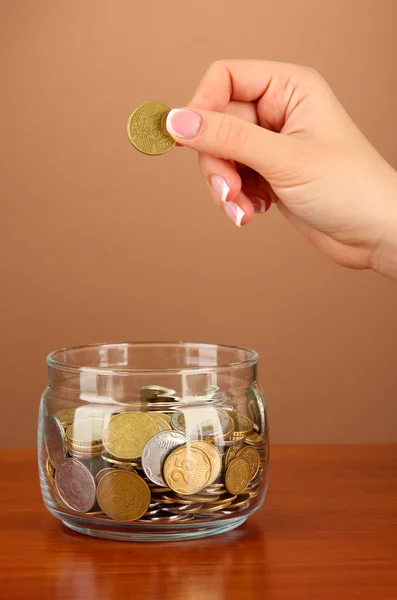 Sparen, weibliche Hand steckt eine Münze in Glasflasche, auf farbigem Hintergrund — Stockfoto