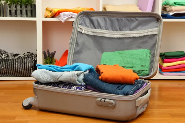 Open grey suitcase with clothing in room — Stock Photo, Image