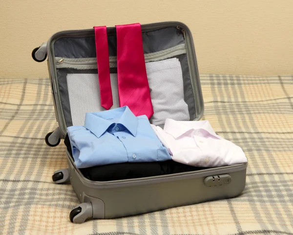 Open grey suitcase with clothing on bed — Stock Photo, Image