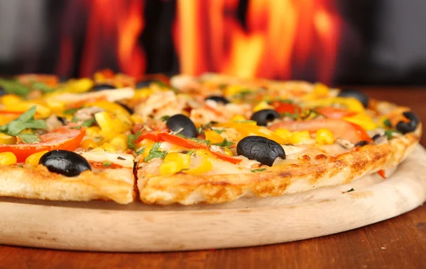 Delicious pizza close-up on wooden table on fire background — Stock Photo, Image