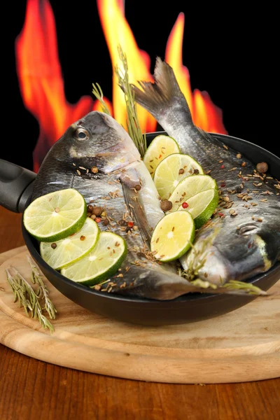 Two fish dorado with lemon on pan on wooden table on fire background — Stock Photo, Image