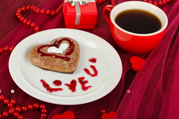 Biscoito de chocolate em forma de coração com xícara de café na toalha de mesa rosa close-up — Fotografia de Stock
