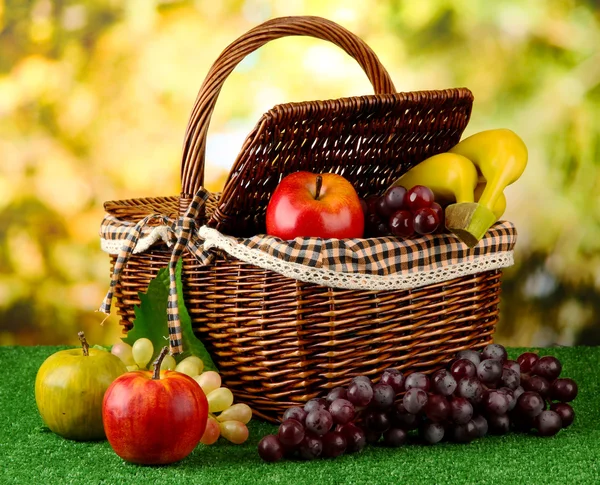 Picnic basket with fruits on grass on bright background — Stock Photo, Image