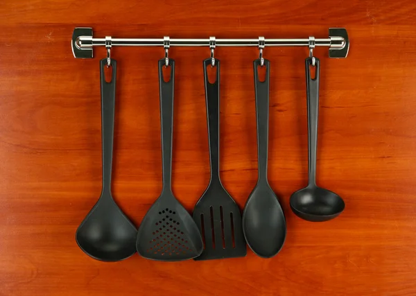 Černá kuchyně nádobí na stříbrné háčky, na dřevěné pozadí — Stock fotografie