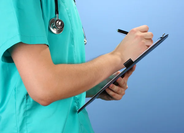 Hand of doctor with pen writing on prescription blank, on blue background