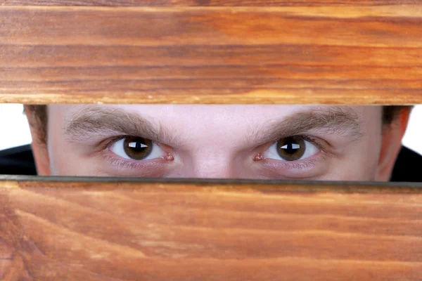 Man eyes looking through hole in wooden desk Royalty Free Stock Photos