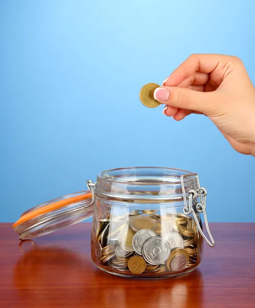 Sparen, weibliche Hand steckt eine Münze in Glasflasche, auf farbigem Hintergrund — Stockfoto