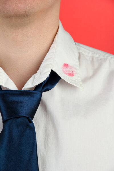 Lipstick kiss on shirt collar of man, on red background