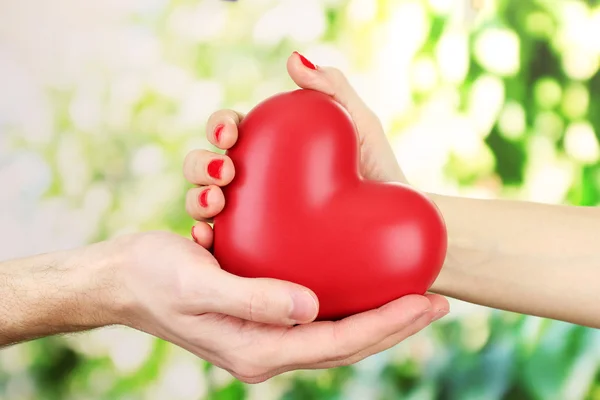 Corazón rojo en manos de hombre y mujer, sobre fondo verde — Foto de Stock