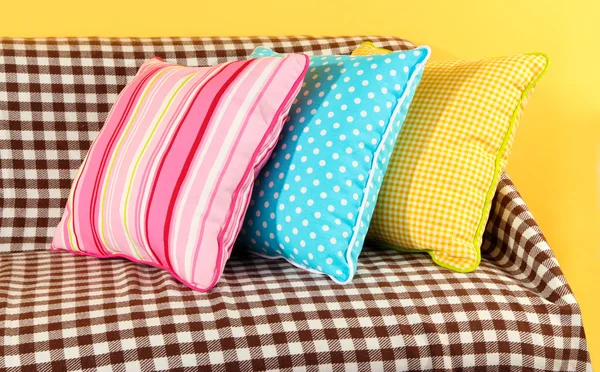 Colorful pillows on couch on yellow background — Stock Photo, Image