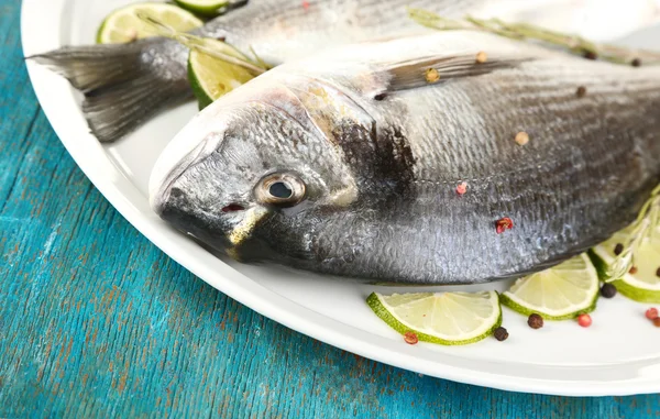 Two fish dorado with lemon on plate on blue wooden table close-up — Stock Photo, Image