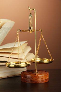 Gold scales of justice and books on brown background clipart