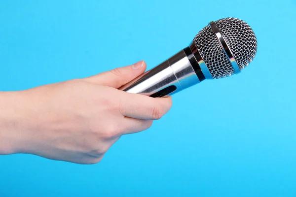 Silbernes Mikrofon in der Hand auf blauem Hintergrund — Stockfoto