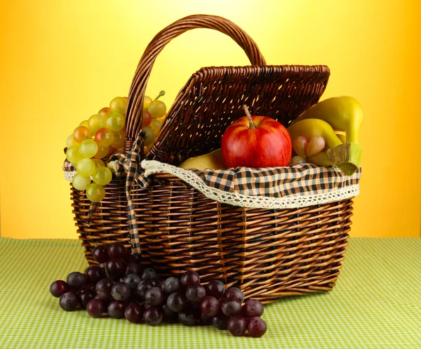 Picnic basket with fruits on cloth on yellow background — Stock Photo, Image