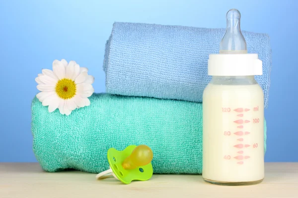 Baby bottle of milk with pacifier and towels on blue background — Stock Photo, Image