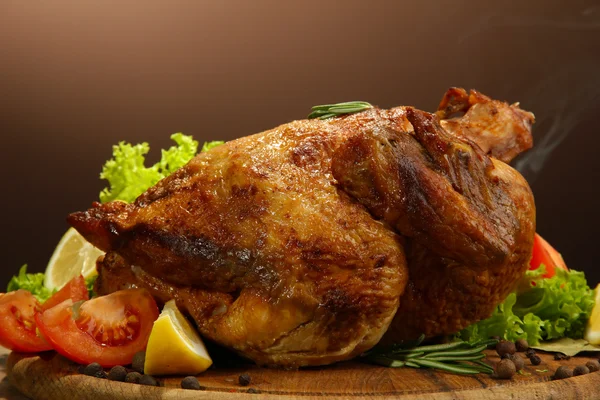 Geheel gebraden kip met groenten, op houten tafel, op bruine achtergrond — Stockfoto