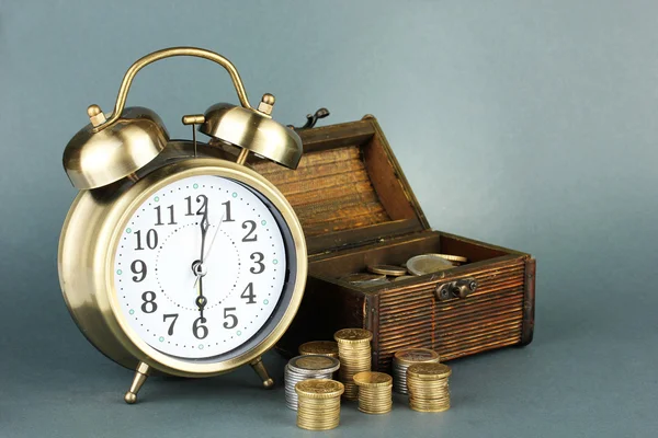 Reloj despertador con monedas en el pecho sobre fondo gris —  Fotos de Stock