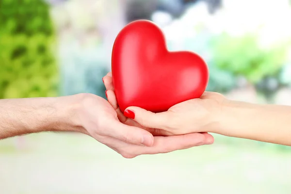 Red heart in woman and man hands, on green background — Stok Foto