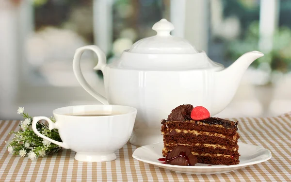 Чайник, чашка чая и вкусный торт на фоне окна — стоковое фото