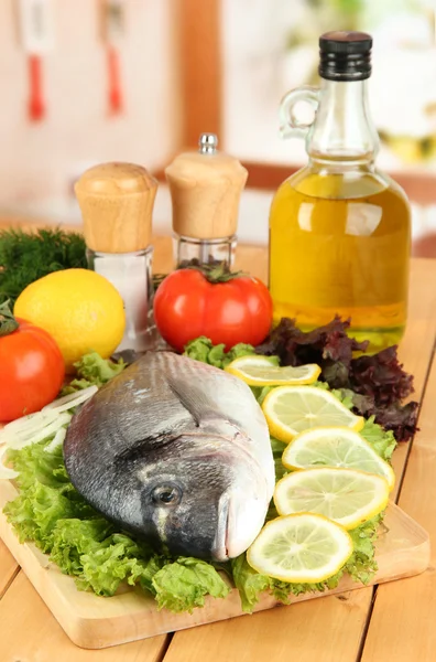 Dorado fresco sobre tabla de cortar con limón y verduras sobre mesa de madera —  Fotos de Stock