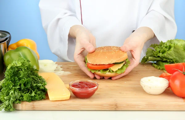 Mâinile de sex feminin pregătesc cheeseburger, pe fundal albastru — Fotografie, imagine de stoc