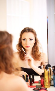 Genç ve güzel bir kadın aynanın yanında makyaj yapıyor.