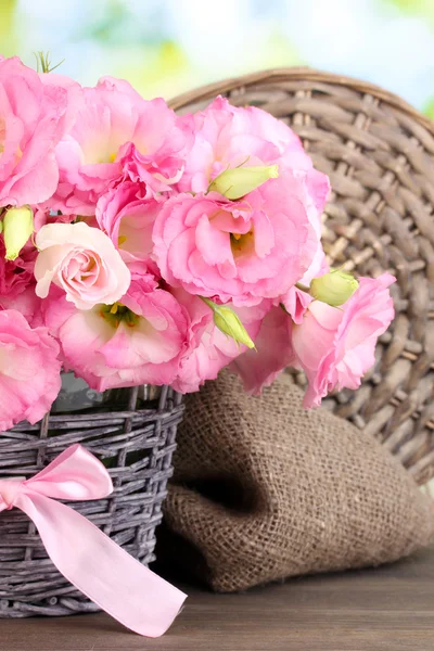 Strauß Eustoma-Blumen in Korbvase, auf Holztisch, auf grünem Hintergrund — Stockfoto